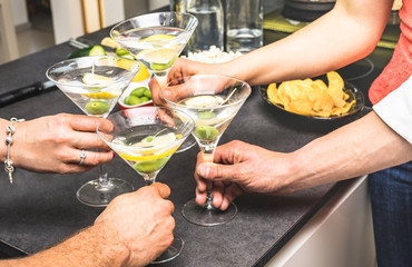 Hands of friends having fun at house party with pre dinner aperitif martini cocktails and chips olives snacks - Young people spending time together at home - Birthday event celebration concept