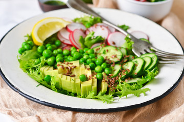 Mix salad with cucumber, avocado, green peas and flax seeds on a marble background