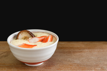 homemade style steamed egg with crab stick and shiitake mushroom in a white ceramic bowl on wooden table. healthy food concept.