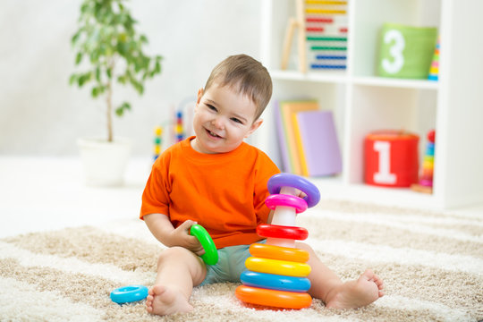 Baby toddler boy playing indoors with developmental toy sitting on soft carpet