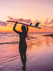 Surffrau geht zum Surfen. Mädchen mit Surfbrett an einem Strand bei Sonnenuntergang oder Sonnenaufgang. © artifirsov