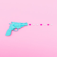 blue plastic gun shoots a pink and white bullets on pink background. minimal. creative concept