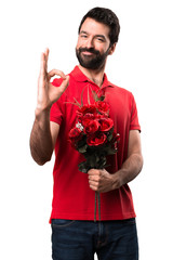 Handsome man holding flowers making OK sign over white background