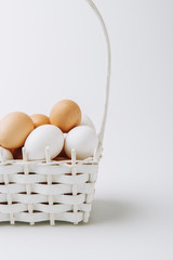 white and brown eggs laying in wicker basket on white background