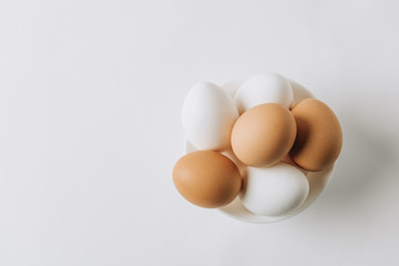 top view of white and brown eggs laying on white plate on white background