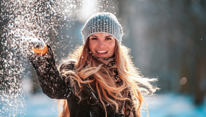 Naklejka premium Smiling young woman throwing snow in the air looking at camera