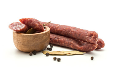 Three Hungarian dry sausages pepperoni with black pepper and bay leaves cut pieces in a wooden bowl isolated on white background smoked in natural casing mixed pork and beef.