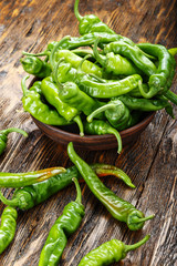 green chili peppers placed in a clay plate on a brown wooden table. with space for text