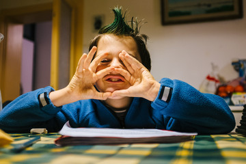 portrait of 9 year old boy at home with crest of green colored hair, performs funny gestures on the...