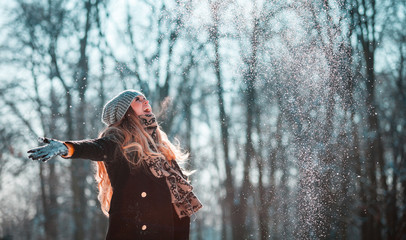 Fototapeta na wymiar Smiling woman throwing snow in the air at sunny winter day