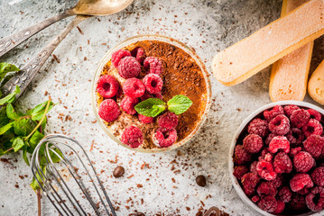 Cooking Italian food dessert Tiramisu, with all the necessary ingredients cocoa, coffee, mascarpone cheese, mint and raspberries, on grey stone background.  Copy space