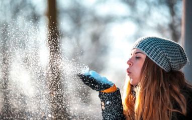 Fototapeta premium Winter woman blowing snow outdoor at sunny day, flying snowflakes