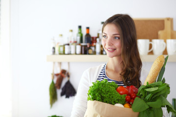Young woman holding grocery shopping bag with vegetables .Standing in the kitchen. Young woman