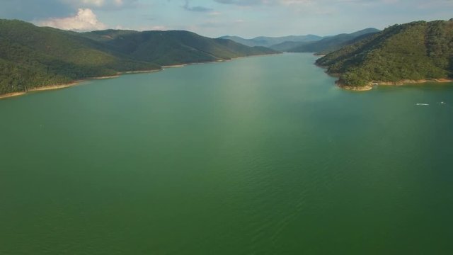 Backward flight over beautfiul lake among green hills at sunset