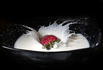 Strawberries fall into milk with a spray