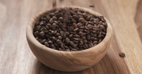 coffee beans falling into wood bowl on table