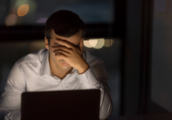 Serious business man working with team till late night in low light from laptop screen with blurred...