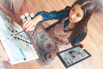 Getting absorbedin the process. Teenager young lady sitting at an easel and holding a tablet...