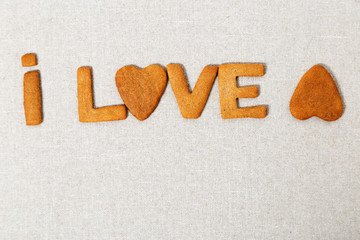 The word Love from homemade shortbread cookies with ginger on linen fabric. Cookies in heart shape. Copy space.