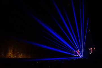 Blue laser rays during a concert in a hangar. Led wall on the stage. Dark background