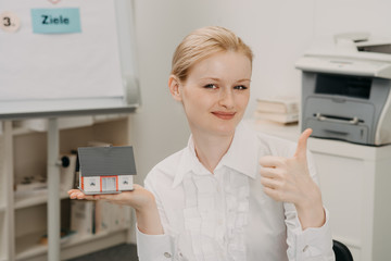 Beautiful woman in office holding model of house. Concept of  property purchase