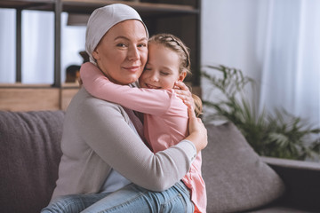 sick mature woman in kerchief hugging cute little granddaughter, cancer concept