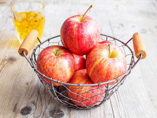 Rote Äpfel in einem Drahtkorb, Apfelsaft im Glas
