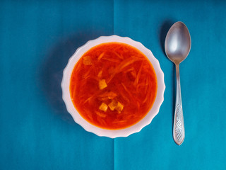 White plate with red home Ukrainian, Russian borscht on a colored background with a metal spoon. Abstract composition on the theme of food, top view. National cuisine, soup with beetroot and cabbage.