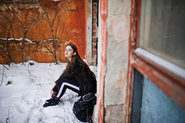 Fototapeta na wymiar Fashionable long legs brunette model in long black cloak posed outdoor at winter day against old grunge wall.