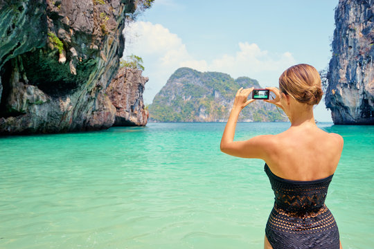 Tourism and vacation in Thailand. Pretty young woman taking picture of beautiful landscape on tropical beach.