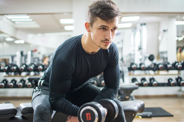 Fototapeta na wymiar Handsome young man lifting dumbbell at gym.