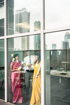 Three Indian employees sticking reminders on glass wall with business tasks and deadlines in the office