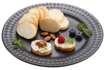 Sandwiches with mascarpone cream cheese, fresh berries and nuts on a black plate. Isolated on a white background.