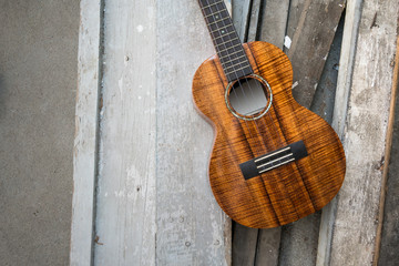 Curly koa ukulele gloss finished against wooden background.