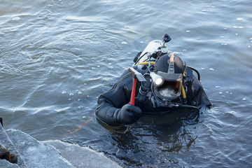 Fototapeta na wymiar industrial diver with scuba gear and hammer working in the water at the shore reinforcement, copy space