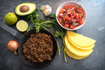 ingredients for mexican tacos with roasted beef tomatoes and avocado on a dark stone background, top view from above