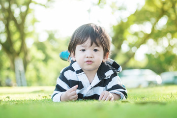 Closeup asian kid lied on grass floor in the garden with sun light background with cute motion