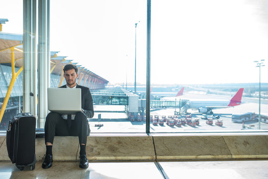 young handsome businessman using his laptop and mobile phone at the airport waiting for his flight and smiling