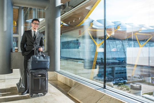 handsome young businessman smiling next to the window with his baggage waiting for his flight