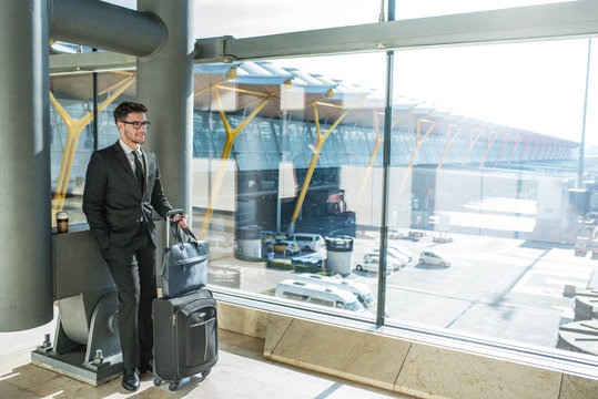 handsome young businessman smiling next to the window with his baggage waiting for his flight