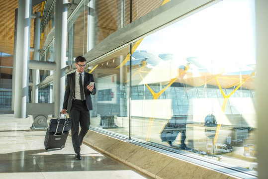 young businessman walking at the airport using his mobile phone