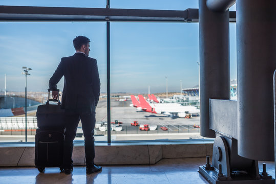 businessman standing at the airport window waiting for his flight with luggage