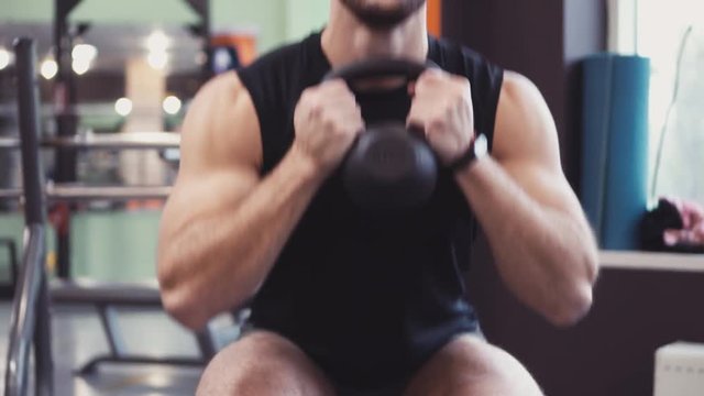 Young fit man at gym doing squats on fitness ball