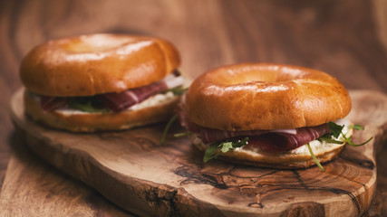 two bagels with prosciutto and cream cheese on wood boar