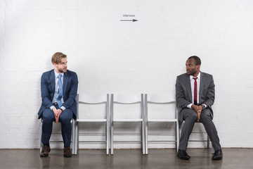 scared multiethnic businessmen looking at each other while waiting for job interview
