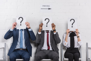 obscured view of multicultural business people holding cards with question marks while waiting for job interview