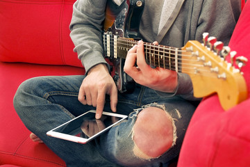 Casually dressed young man with guitar playing songs in the room at home. Online guitar lessons...