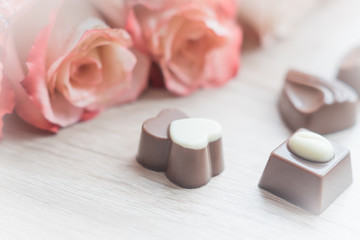 chocolate sweets and pale roses on wooden table, toned