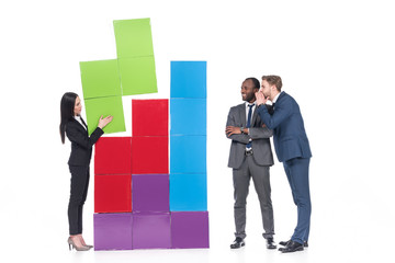 multicultural businessmen looking at asian businesswoman collecting colorful blocks isolated on white