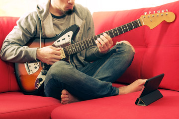 Casually dressed young man with guitar playing songs in the room at home. Online guitar lessons...